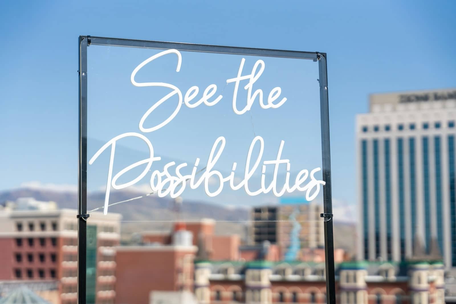 Neonschriftzug „See the Possibilities“ vor einer Stadtkulisse