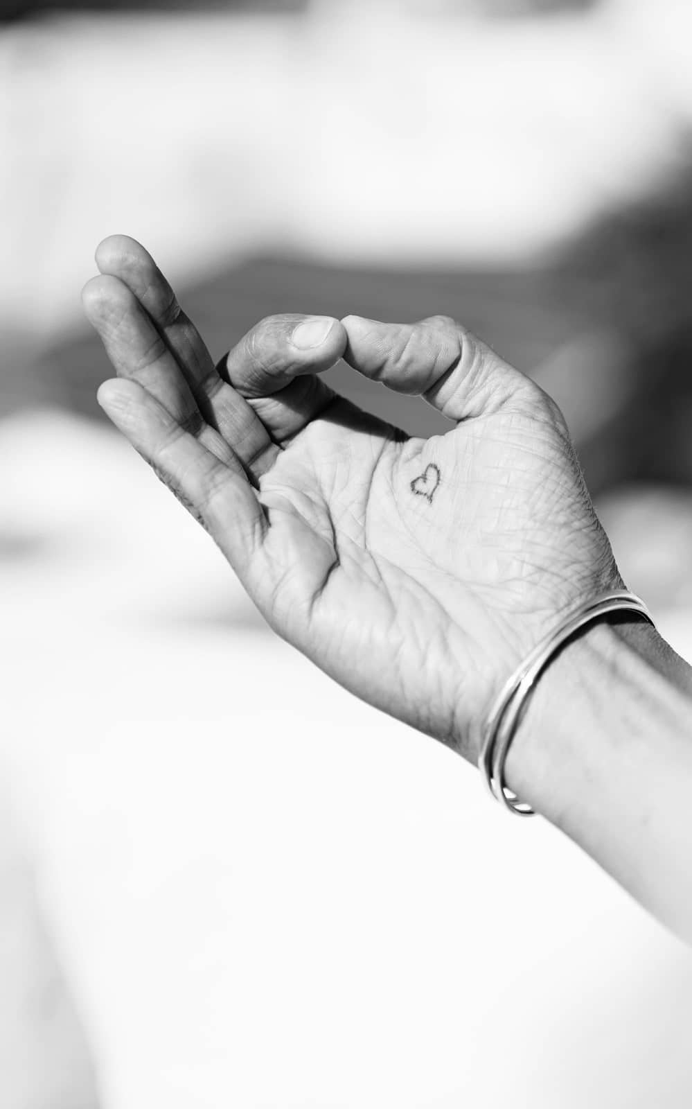 Hand in Mudra-Haltung mit kleinem Herz-Tattoo und Armreif