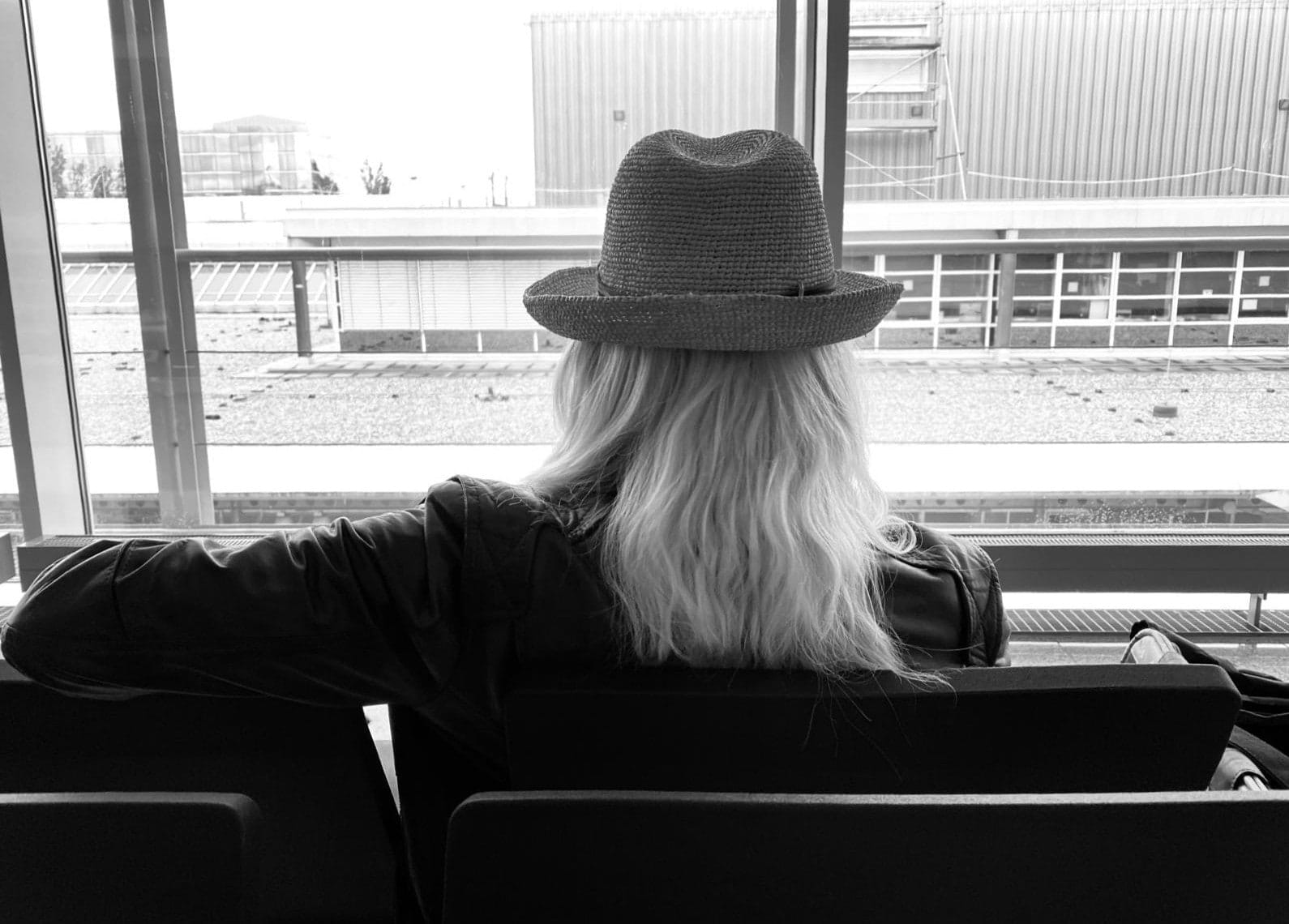 Tina Maria Werner mit Hut von hinten, sie blickt aus einem großen Fenster (Schwarz-Weiß)
