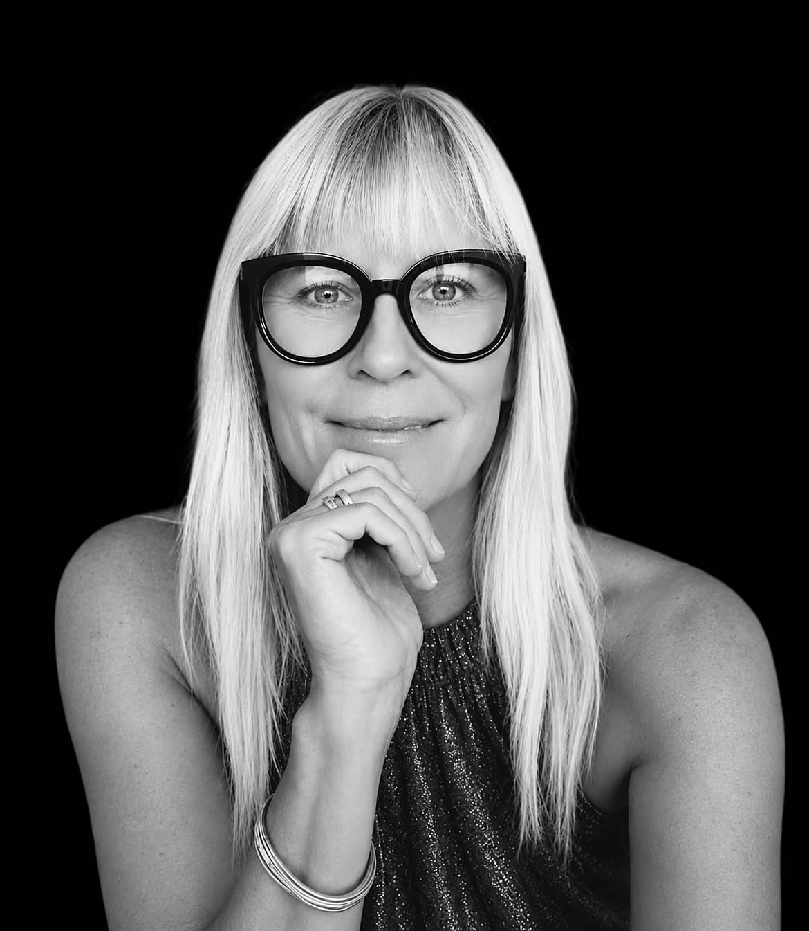 Tina Maria Werner mit Brille, lächelnd, die Hand am Kinn – Schwarz-Weiß-Porträt